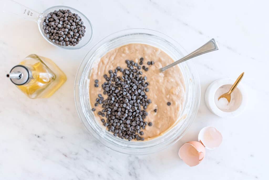 Banana muffin batter in a glass mixing bowl with chocolate chips about to be folded in.