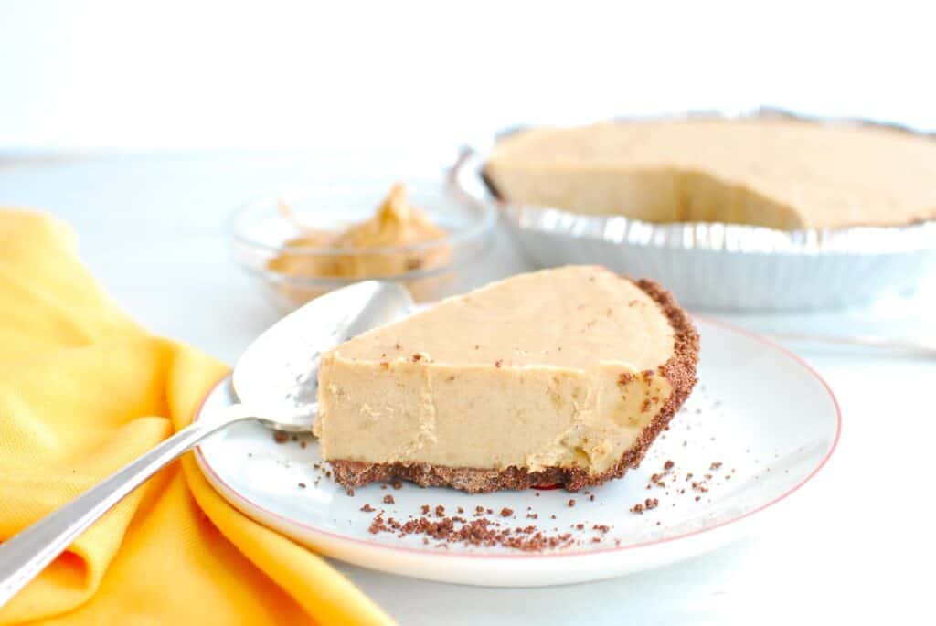 A slice of dairy free peanut butter pie on a white plate next to a yellow napkin and a spoon.