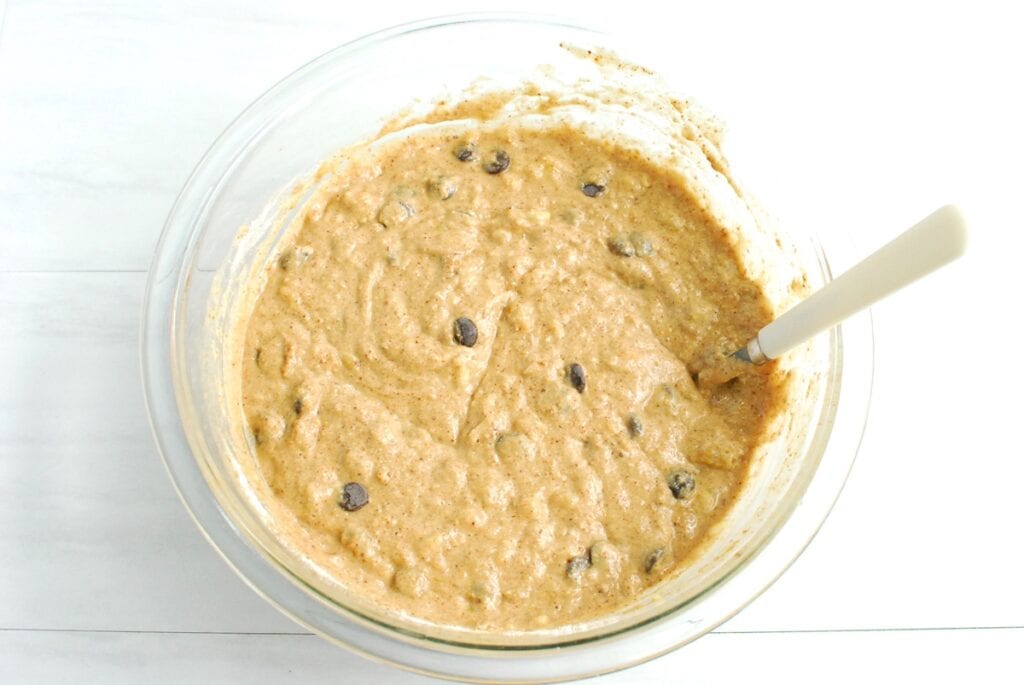 Muffin batter with chocolate chips folded in, in a glass mixing bowl.