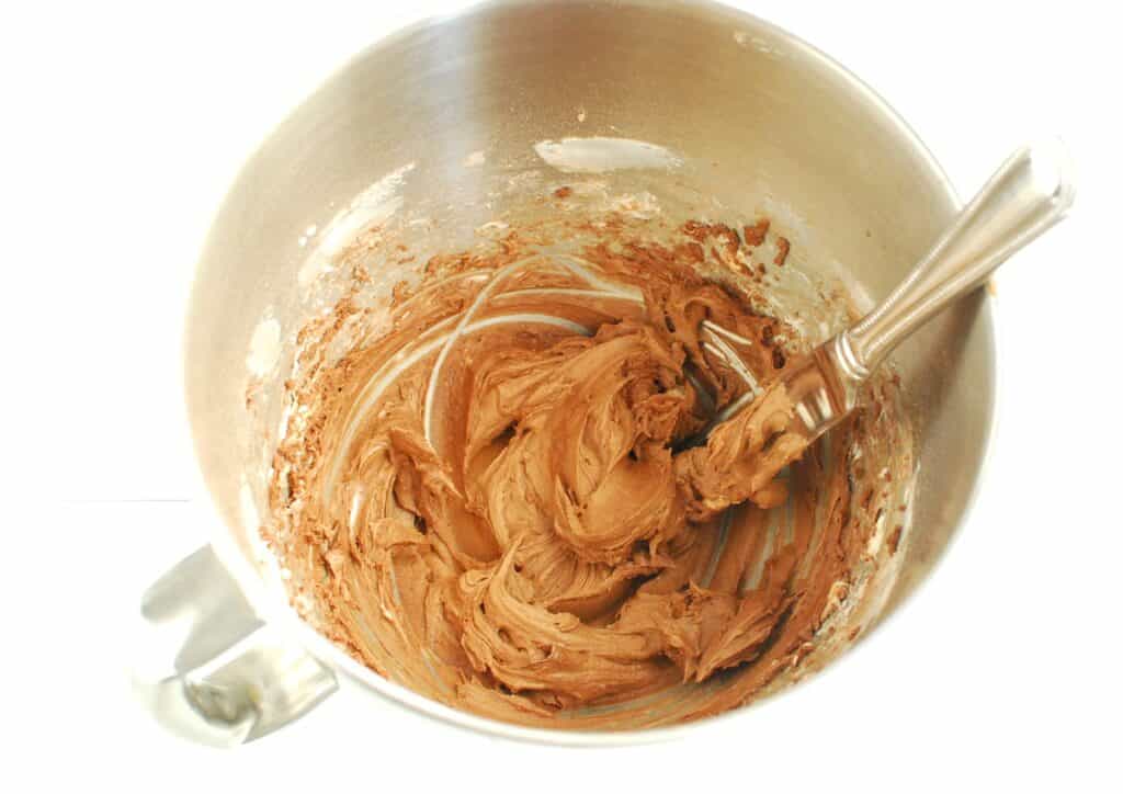 Dairy-free butter, powdered sugar, oat milk, and cocoa powder mixed into frosting in a mixing bowl.
