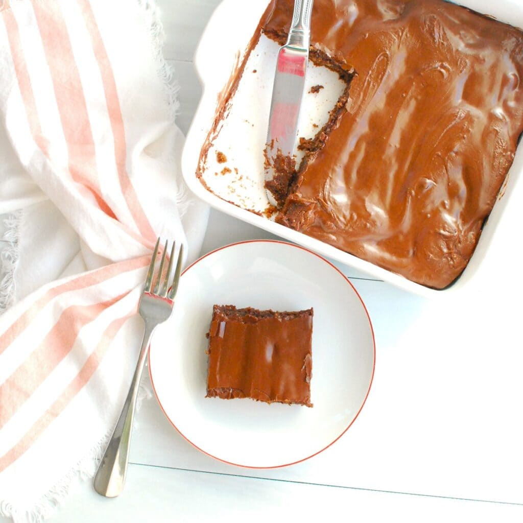 A brownie on a plate next to a baking dish full of brownies, all topped with chocolate frosting.
