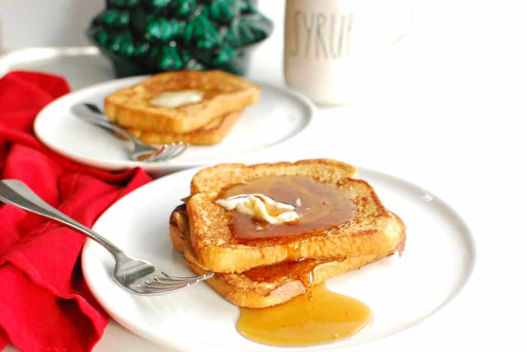 Two slices of dairy free eggnog French toast on a white plate, with another plate in the background.