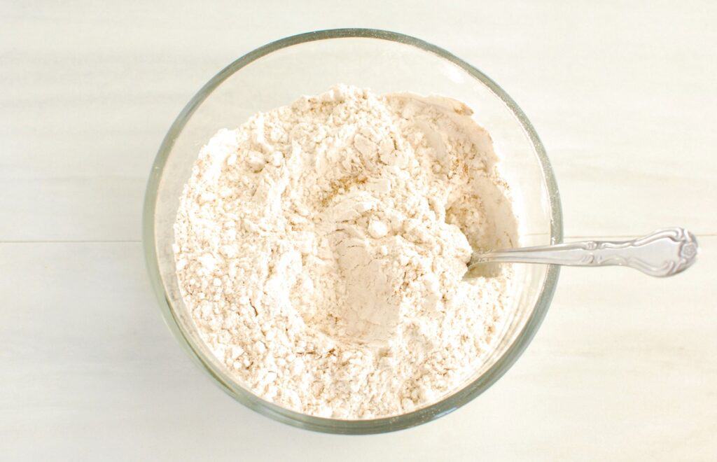 Flour, cinnamon, ginger, cloves, nutmeg, baking soda, and salt mixed together in a glass bowl.