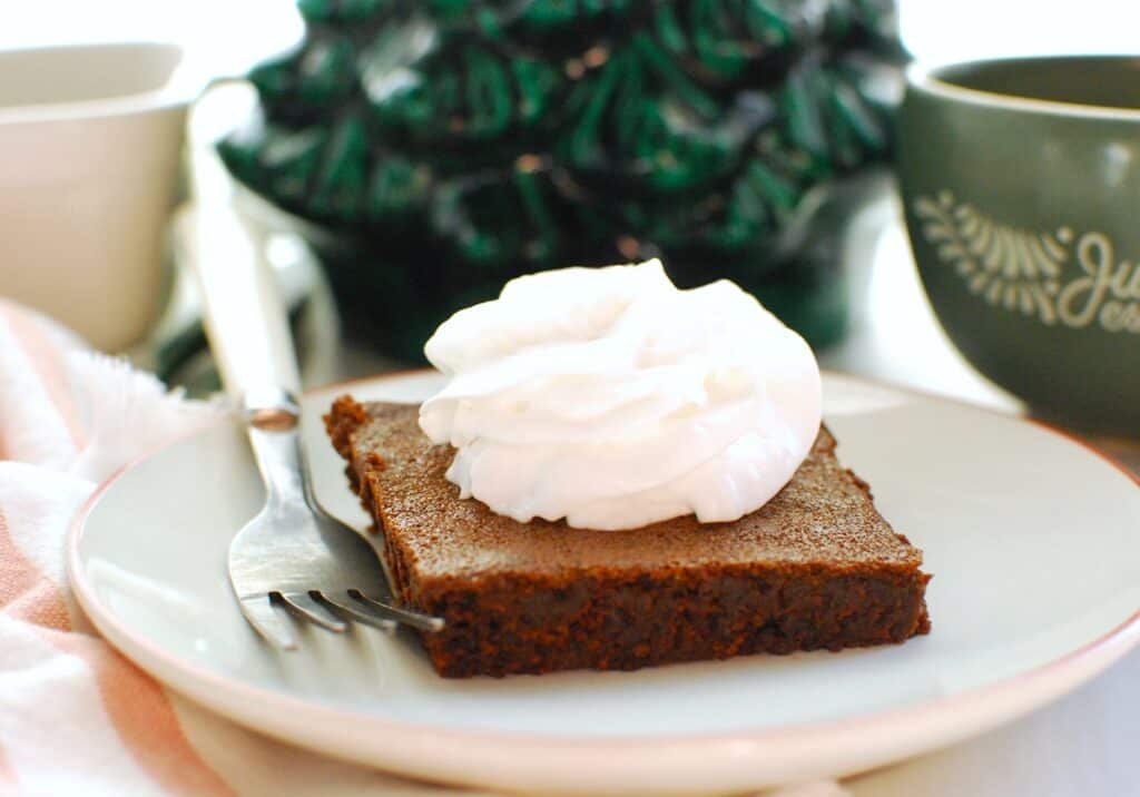 A gingerbread brownie on a plate with Christmas decorations in the background.