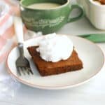 A gingerbread brownie on a white plate topped with dairy free whipped cream.