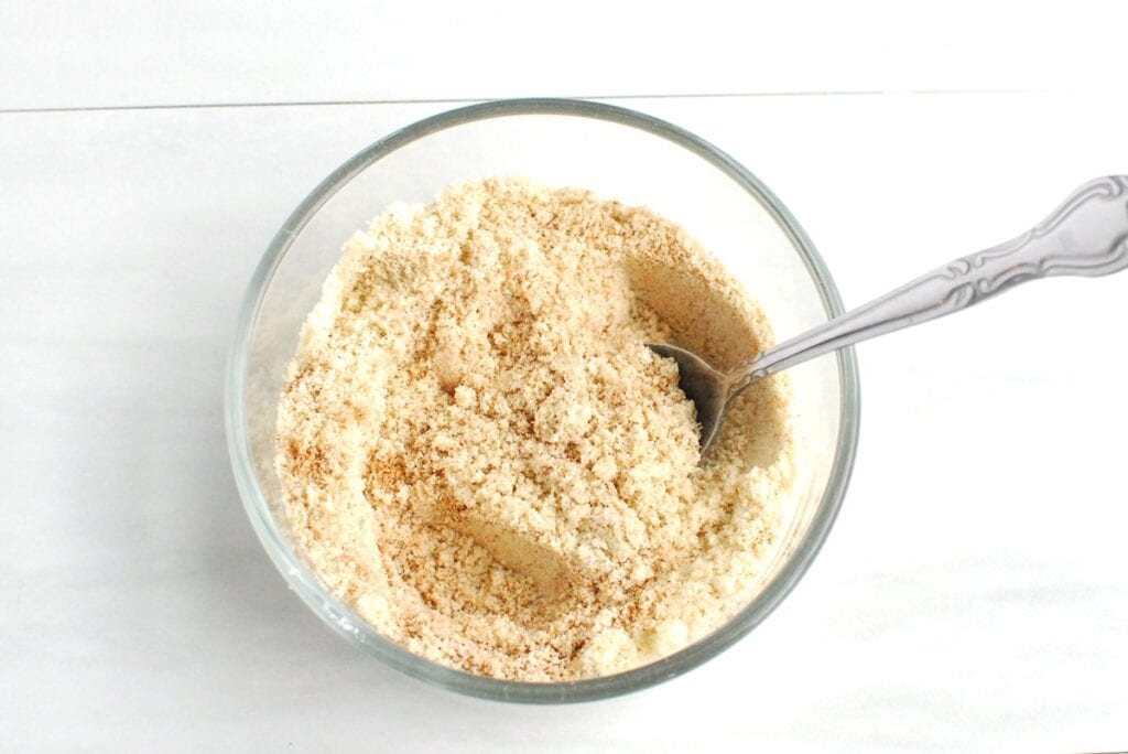 Almond flour, baking powder, cinnamon, cardamom, ginger, cloves, and salt mixed together in a bowl.