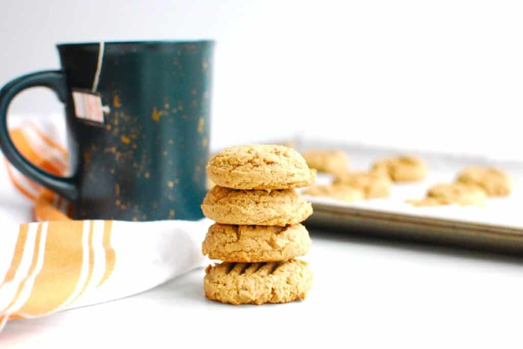 A stack of four chai cashew cookies with a coffee mug in the background.