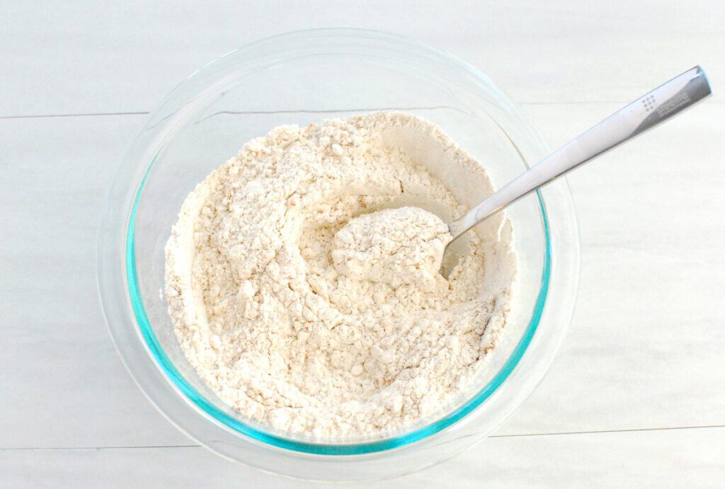 Flour, cinnamon, ginger, cardamom, cloves, allspice, baking powder, baking soda, and salt mixed together in a bowl.