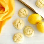 Four lemon rosemary olive oil cookies next to a napkin and fresh lemons.