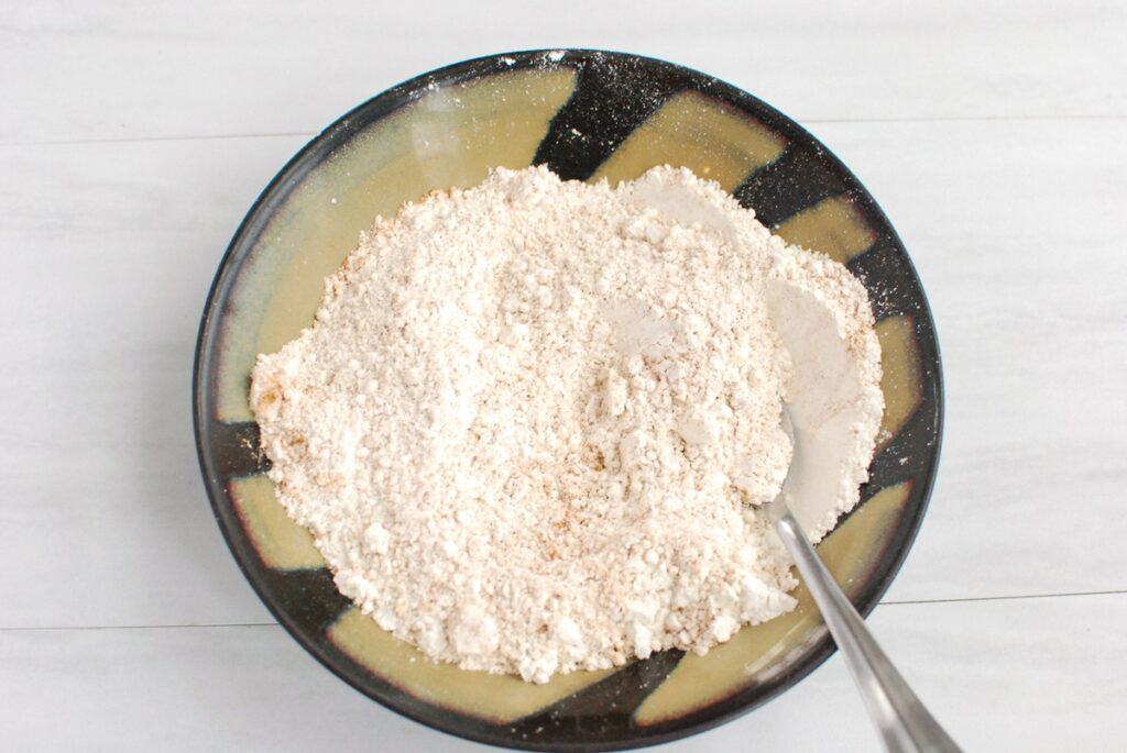 Flour, cinnamon, nutmeg, baking powder, baking soda, and salt mixed together in a bowl.