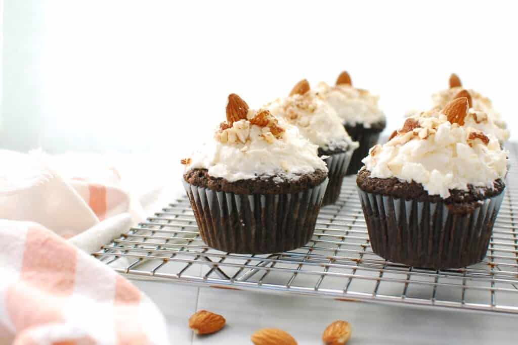 Several dairy free chocolate coconut cupcakes on a cooling rack next to a napkin.