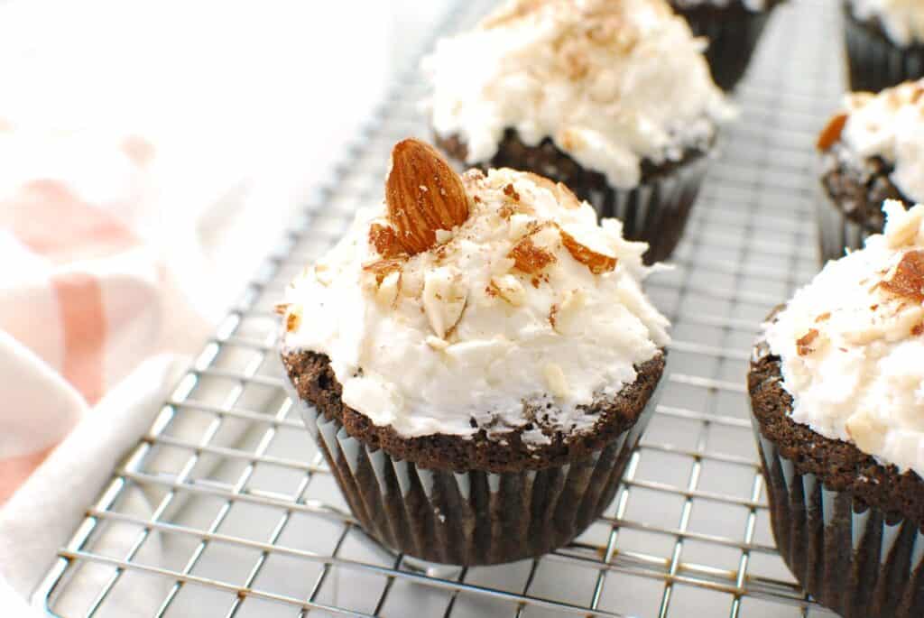A dairy free almond joy cupcake on a cooling rack, garnished with almonds.