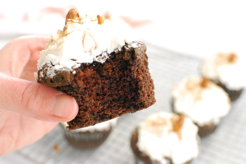 A woman's hand holding a cupcake with a bite taken out of it.