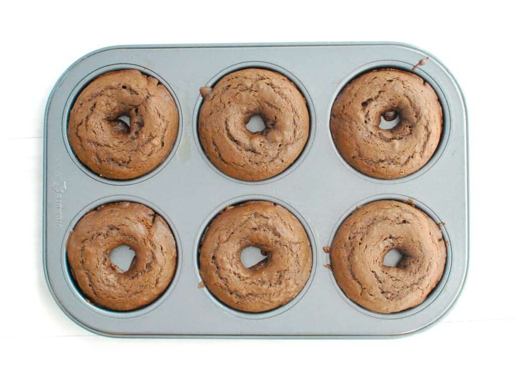 Just-baked chocolate donuts in a donut tin.