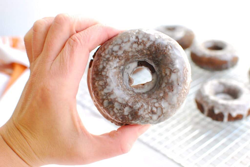 A woman's hand holding a chocolate glazed donut.