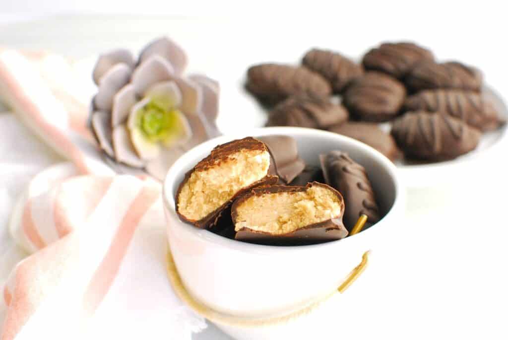 Several dairy free chocolate peanut butter eggs in a bowl, with one split in half showing the peanut butter filling.
