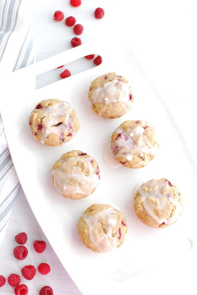 Six raspberry muffins with glaze on top on a white platter.