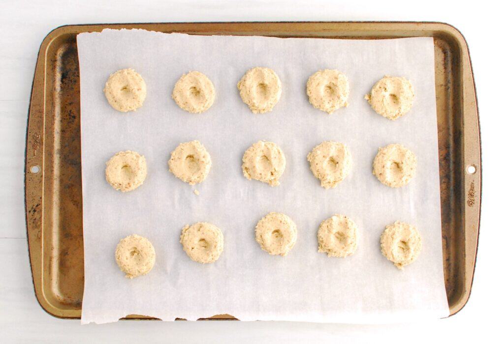 Cookie dough portioned onto a parchment-lined baking sheet with a thumbprint made in each one.