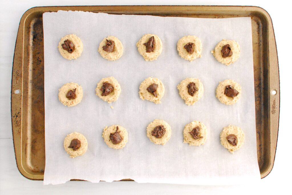 Chocolate hazelnut spread put into the thumbprint of each piece of cookie dough.