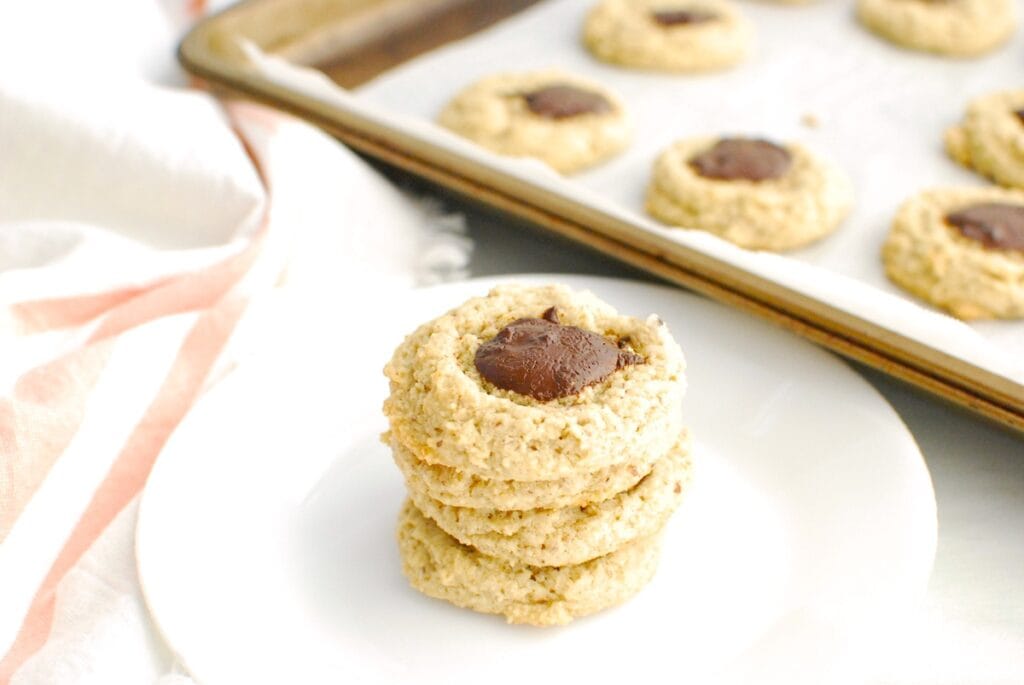 A stack of almond oat thumbprint cookies filled with a chocolate hazelnut spread in the center.