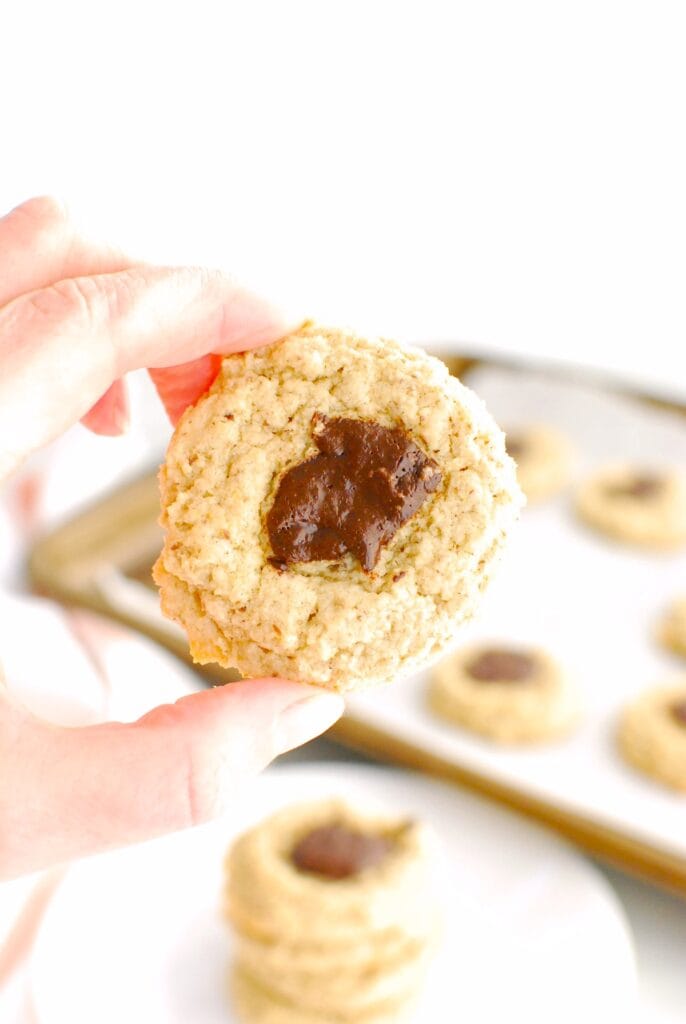 A woman's hand holding a almond oat thumbprint cookie.