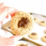 A woman's hand holding a almond oat chocolate thumbprint cookie.