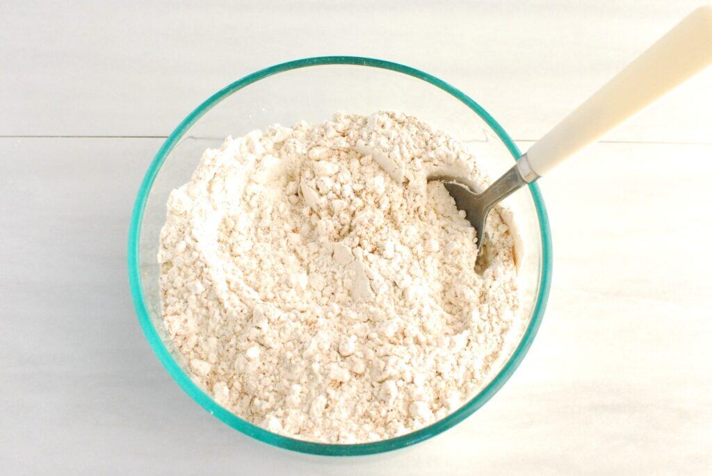 Flour, baking soda, cinnamon, ginger, nutmeg, and salt mixed together in a glass mixing bowl.