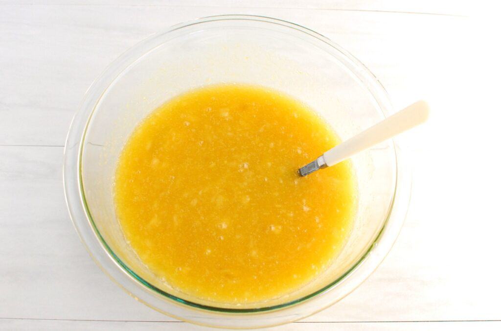 Brown sugar, granulated sugar, vegetable oil, crushed pineapple, eggs, and vanilla mixed together in a glass mixing bowl.