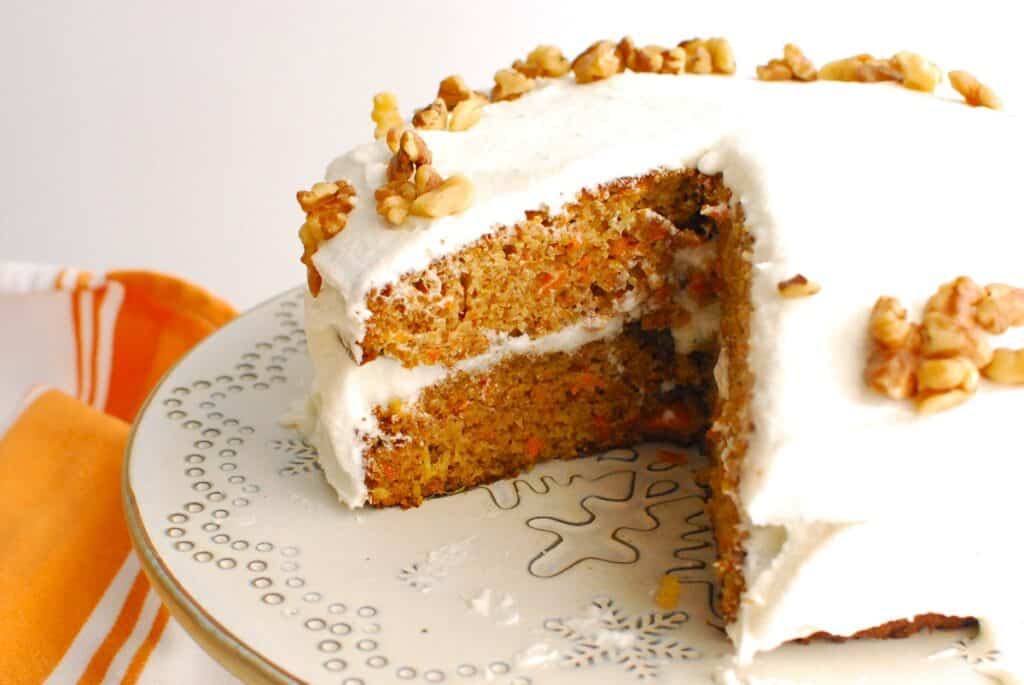 A dairy-free carrot cake on a cake stand with a slice cut from the center.