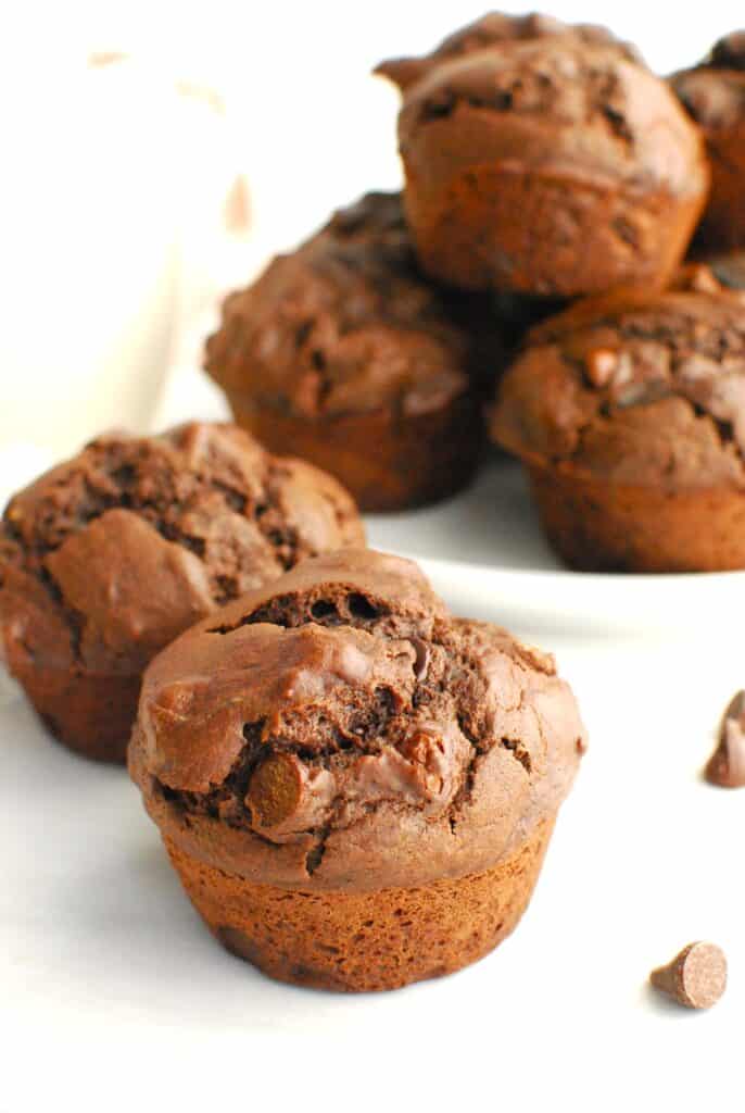 A double chocolate dairy free muffin next to a plate stacked with muffins.