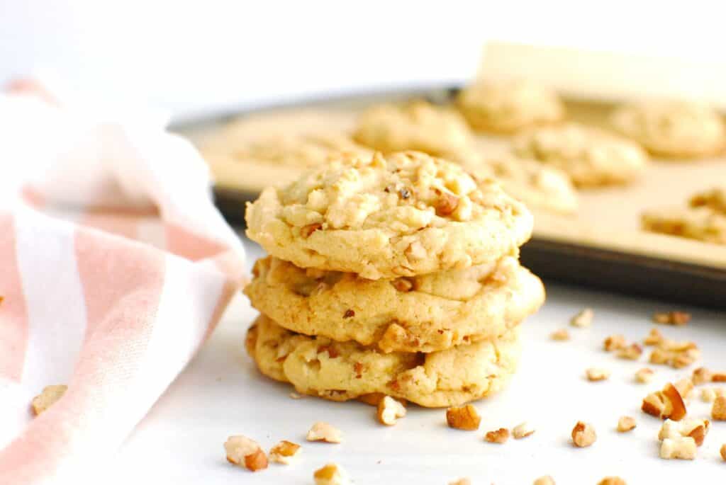 Several dairy free butter pecan cookies next to a napkin with a baking sheet in the background.