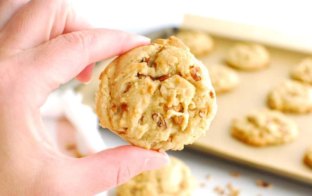 A woman's hand holding a dairy free butter pecan cookie.