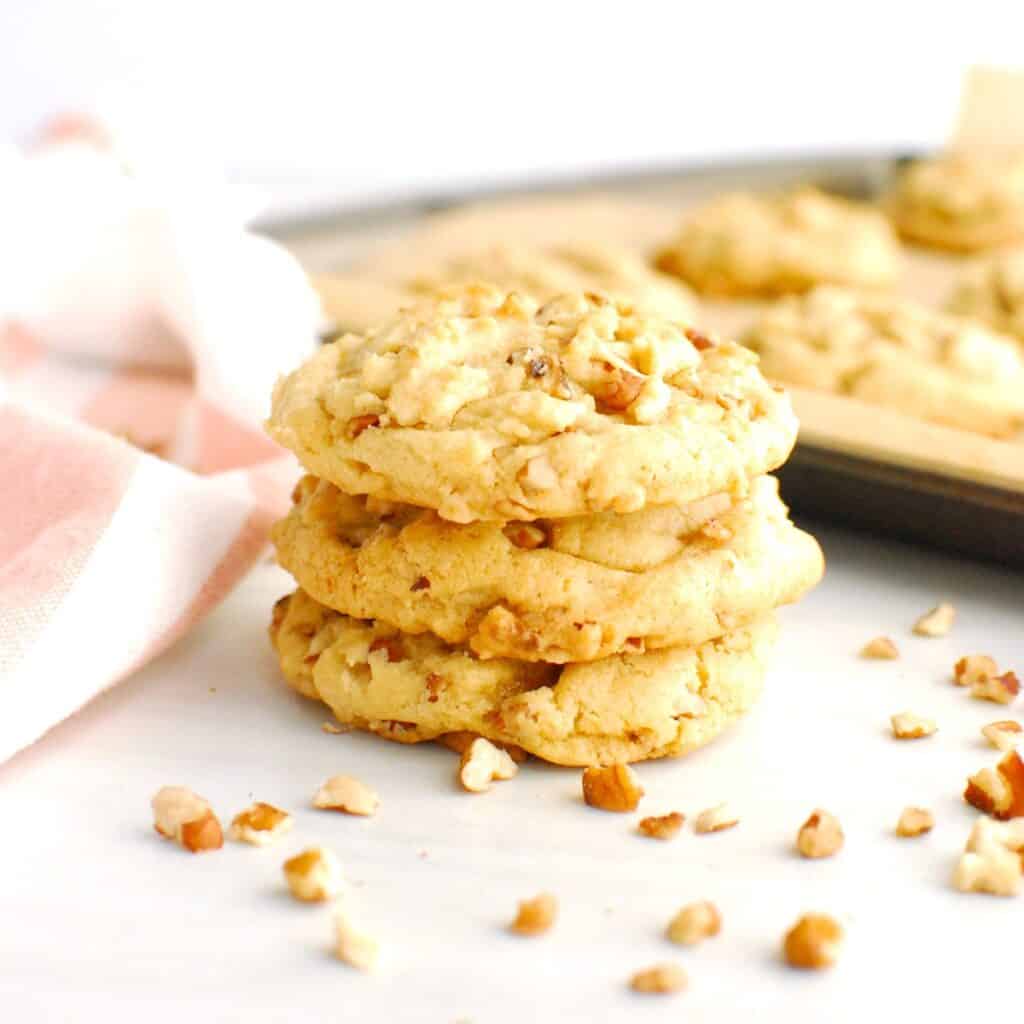 A stack of three dairy free butter pecan cookies on a white table.