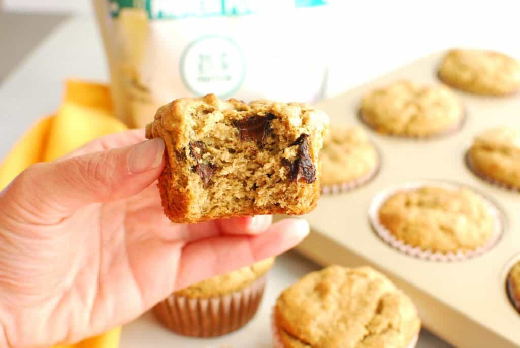 A woman's hand holding a banana protein muffin with a bite taken out of it.