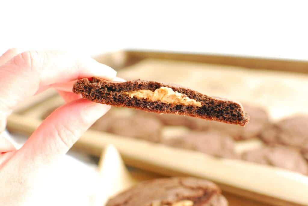 A woman's hand holding a dairy free chocolate cookie stuffed with peanut butter.