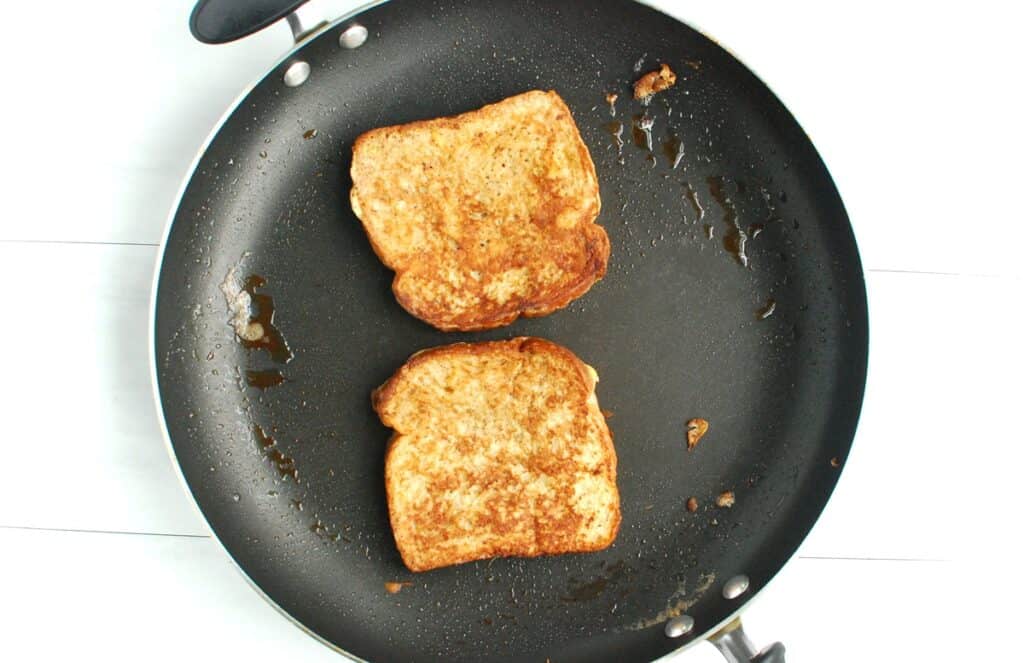 Two slices of french toast cooking in a pan.