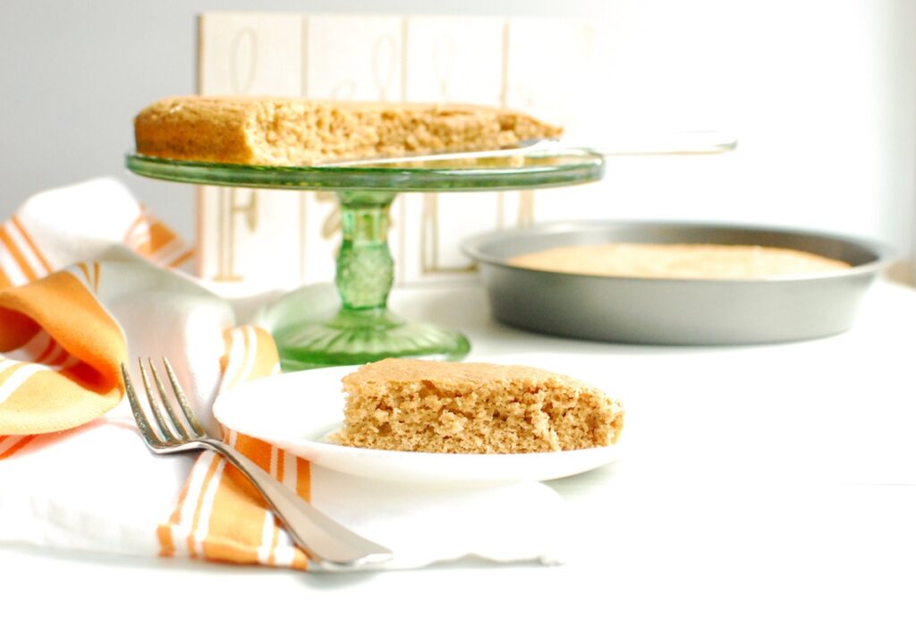 A slice of two ingredient spice cake on a white plate with the rest of the cake in the background.