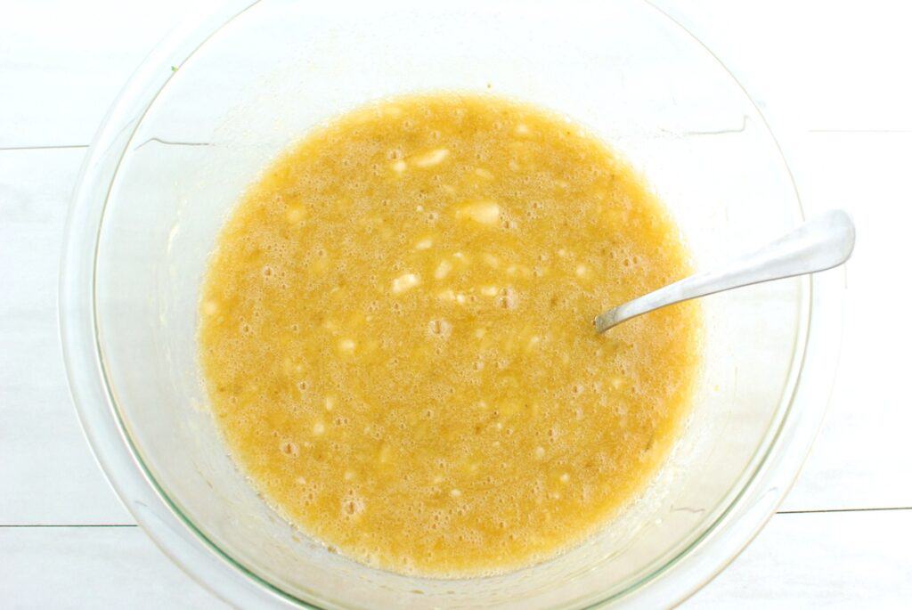 Mashed bananas, eggs, brown sugar, vegetable oil, and vanilla combined in a glass mixing bowl.