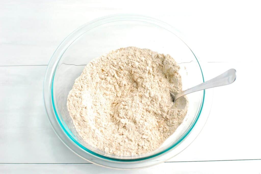 Whole wheat flour, oats, pumpkin spice, baking soda, baking powder, and salt combined in a glass bowl.
