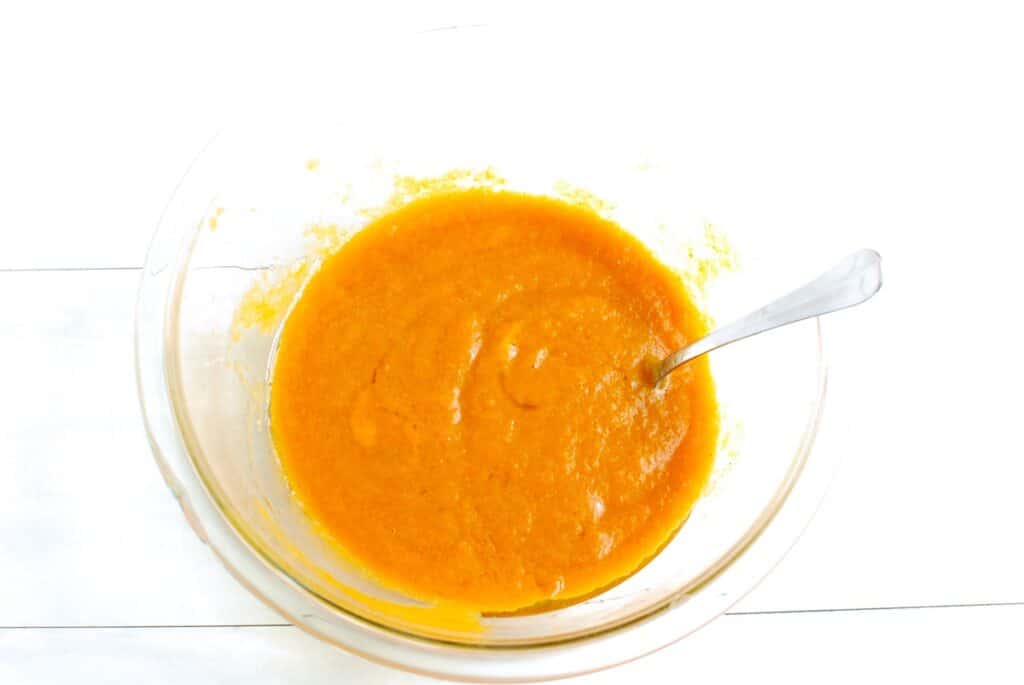 Pumpkin, maple syrup, olive oil, and egg mixed together in a glass bowl.