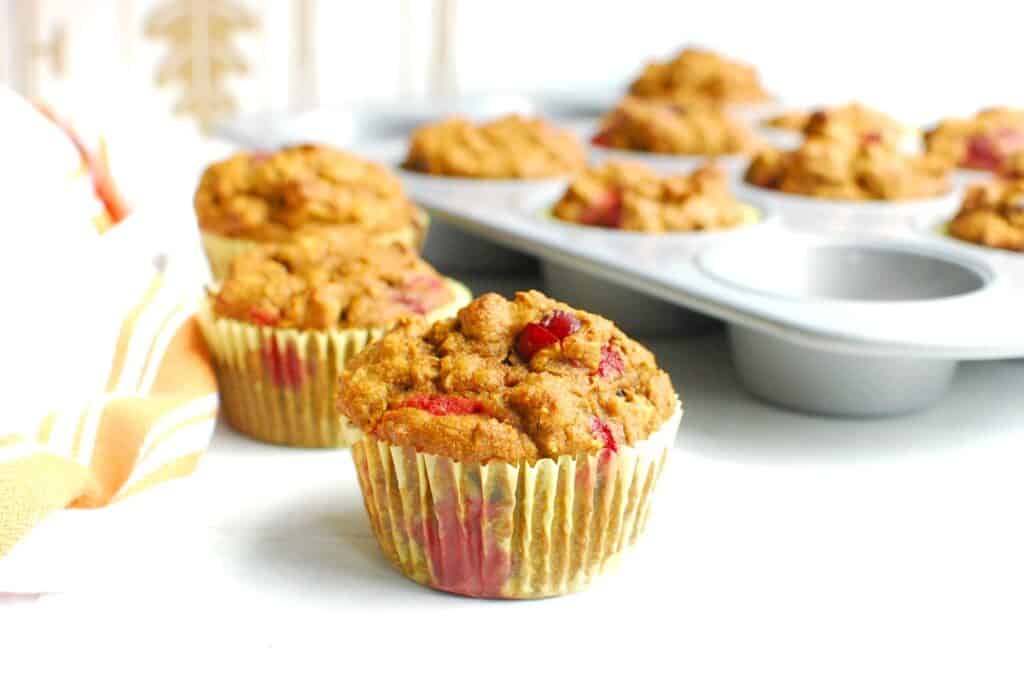 Several pumpkin cranberry muffins on a table with the muffin tin in the background.