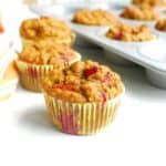 Three pumpkin cranberry muffins on a white table.