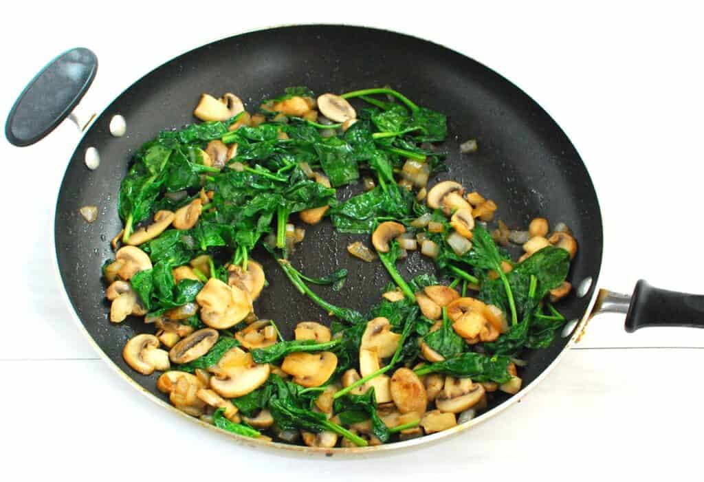 Onions, mushrooms, and spinach cooked in a skillet.