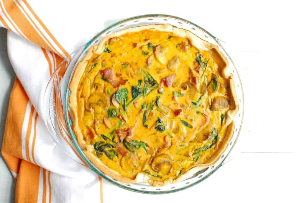 Cooked pumpkin quiche in a glass pie plate.