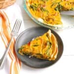 A slice of dairy-free pumpkin quiche on a plate next to a napkin.