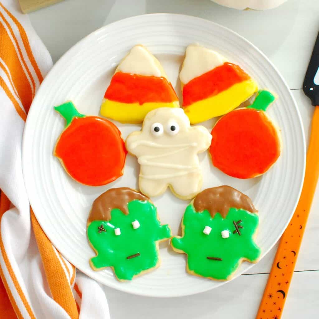 A plate with several dairy free Halloween cookies, including Frankenstein, candy corn, and a mummy.