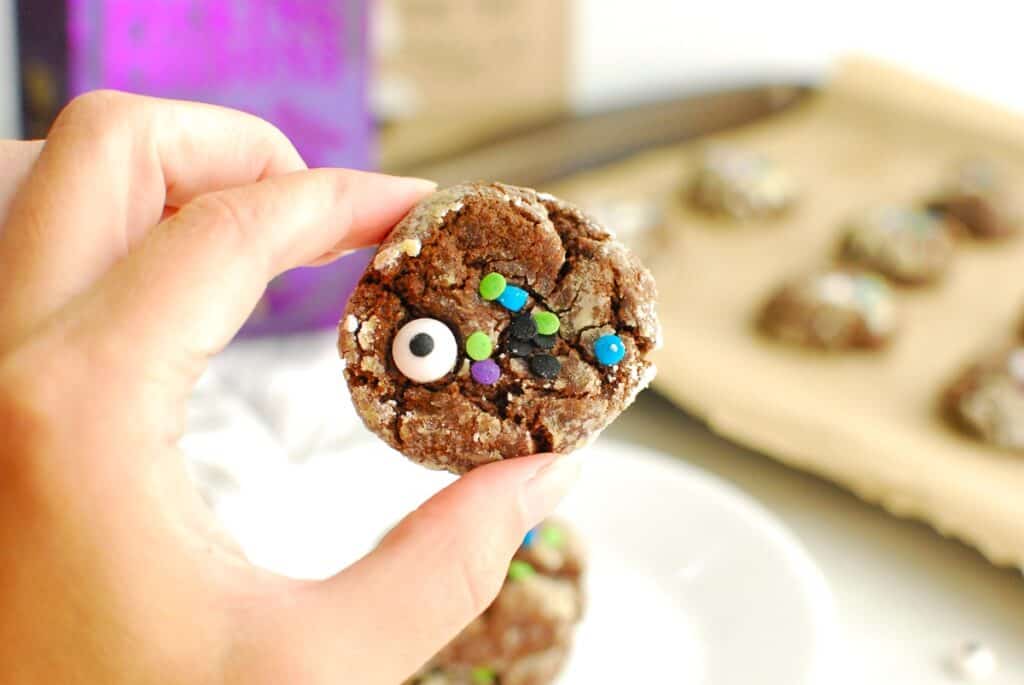 A woman's hand holding a chocolate pumpkin Halloween cookie.