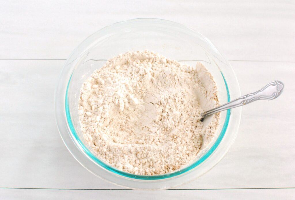 Flour, pumpkin spice, baking powder, baking soda, and salt mixed together in a bowl.