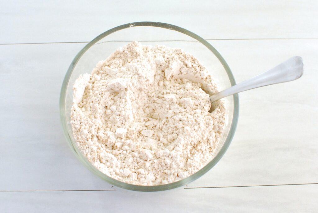 Flour, pumpkin spice, baking soda, and salt mixed together in a glass bowl.