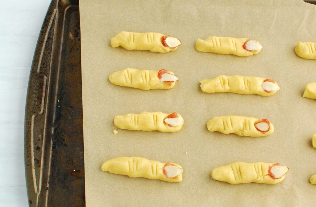 Dough rolled into a finger shape with an almond at the end and knife marks for the knuckles.